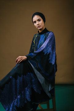 Studio portrait of a tall, slim, elegant and beautiful Middle Eastern Muslim woman in a flowing traditional blue dress with a turban head scarf. She is dressed to celebrate Raya. 