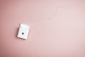 Dental floss in a white plastic container on a pink background. Health concept