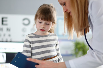 Female doctor listening cute little patient and writing registration information on clipboard pad portrait