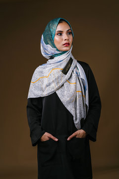 Studio portrait of a tall, slim, elegant and beautiful Middle Eastern Muslim woman in a flowing traditional black dress with a turban head scarf. She is dressed to celebrate Raya.