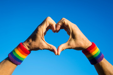 Gay athlete making hand heart with gay pride rainbow colors wristbands against bright blue sky
