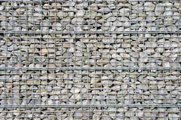 Abstract architectural background of rough retaining wall made from rocks in steel cage gabion baskets
