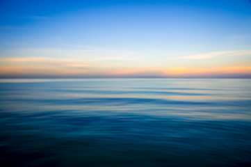 Naklejka na ściany i meble Abstract view of the glassy smooth surface waves of a calm sea during the magic hour of sunrise