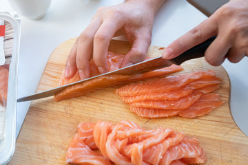 Hand cook using knife slicing a fresh salmon on chopping block