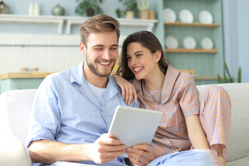 Young couple watching media content online in a tablet sitting on a sofa in the living room.