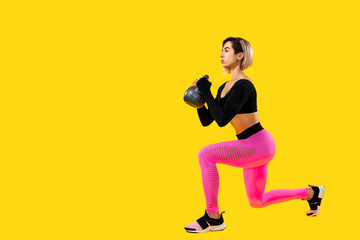 Fototapeta na wymiar Fitness woman in fashionable pink and black sportswear work out with kettlebell on yellow background. Strength and motivation.