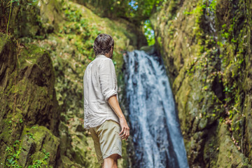 Naklejka premium Happy man enjoying amazing tropical waterfall raised hands Travel Lifestyle and success concept vacations into the wild nature on background mountain