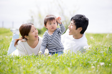 芝生に寝転ぶ若い家族、育児イメージ