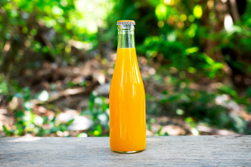 Orange juice packed in glass bottles Table top made of wood and green nature background