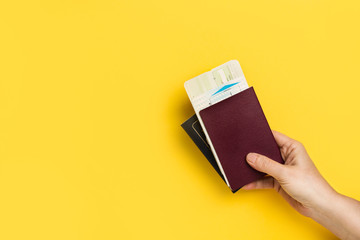 Mano de mujer sosteniendo un pasaporte y billete de viaje sobre un fondo amarillo liso y aislado....