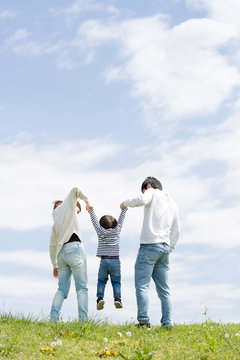 若い家族の全身後ろ姿、青空背景