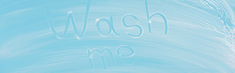 panoramic shot of glass covered with white foam on blue background with wash me lettering