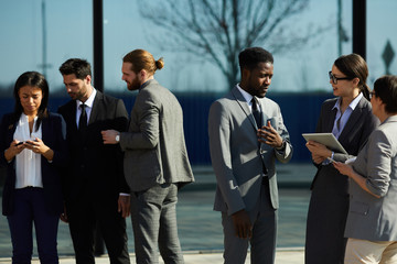 Multi-ethnic business groups standing outdoors and discussing results of research while using modern devices