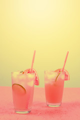 Fresh pink alcoholic cocktail with grapefruit; lemon slice and ice cubes against yellow background
