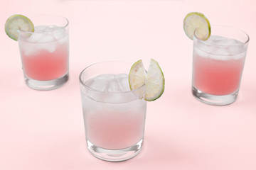 Fresh cocktail with ice cubes and lemon slices against pink background