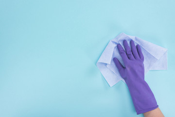 cropped view of cleaner in purple rubber glove holding rag on blue background