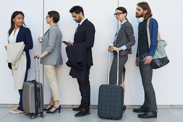 Group of serious boring young multi-ethnic people with bags and luggage standing in line while...