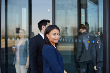 Content beautiful young black woman in dark blue jacket looking at camera while coming in office...