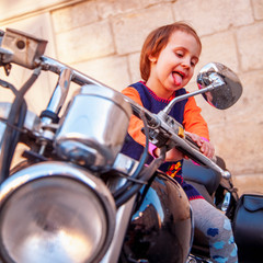 Fototapeta na wymiar Cool little biker child girl playing and having fun on fashioned motorcycle. Humorous photo.
