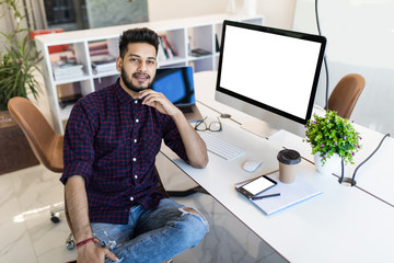 Indian smiling businessman sitting in comfortable chair in front of computer monitor and relaxing...