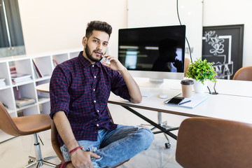 Indian smiling businessman sitting in comfortable chair in front of computer monitor and relaxing...