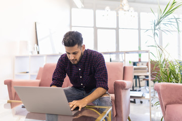 Indian man at home on sofa using a laptop in modern office