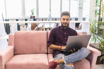 Indian man at home on sofa using a laptop in modern office