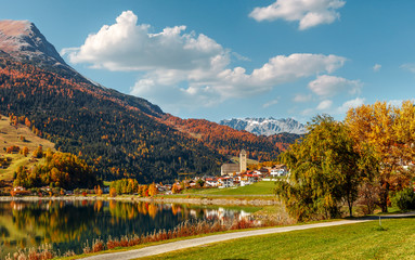 Fototapeta na wymiar Awesome Alpine Highlands and Mountain Lake Resia in Sunny Day. Impressively Beautiful Autumn of Italian Alps and Lago di Resia or Lake Reschen. Tyrol, Italy, Reschensee. Amazing Alpine. Postcard.