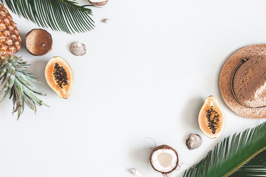 Flat lay photograph with hat, exotic fruit and palm leaves
