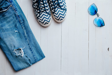 Blue ripped jeans, sunglasses and american star on the white wooden background.