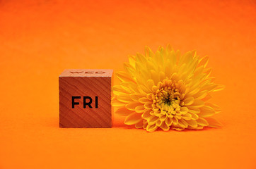 The abbreviation for friday on a wooden block with a yellow daisy on an orange background