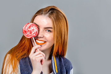 Beautiful woman with lollipop having fun. Playful red hair girl with long hair over grey background 