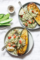 Grilled eggplant with couscous, tomatoes, cilantro with on a light background, top view. Delicious vegetarian lunch. Mediterranean style food