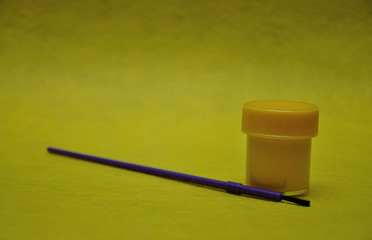A pot of yellow paint with a purple paintbrush on a yellow background