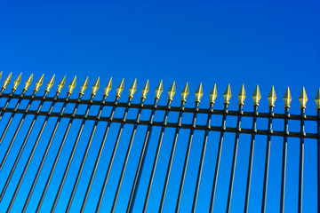 Fence in wrought iron with golden spears on blue sky background