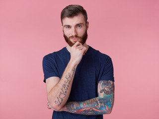 Pensive attractive red-bearded guy with blue eyes, wearing a blue t-shirt, holds his hand at his...