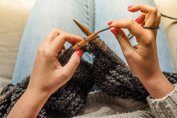 Girl with red nails knitting dark gray wool with wooden needles