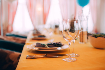 table setting. The dining table is covered with a yellow tablecloth. White plate on a yellow tablecloth. Glass wine glasses on the table.