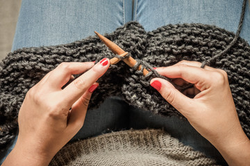 Girl with red nails knitting dark gray wool with wooden needles