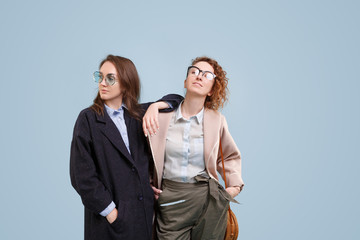 Two young stylish girls - girlfriends posing on a light blue background. Two girls are pleased with the range of a new boutique. Advertising space