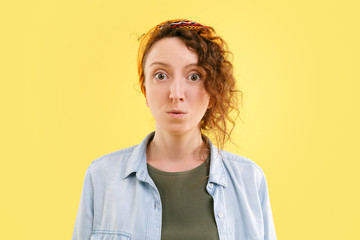 Astonished shocked beautiful young woman dismay looks at the camera and poses on a yellow...