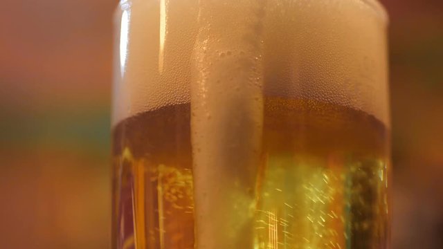 yellow burning beer in huge glass goblet with white foam on top running down on edge close view slow motion