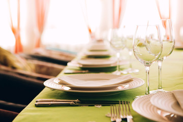 table setting. The dining table is covered with a green tablecloth. White plate on a green tablecloth. Glass goblets on the table. Cutlery. fork, knife, plate, glass.