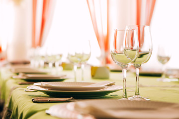 table setting. The dining table is covered with a green tablecloth. White plate on a green tablecloth. Glass goblets on the table. Cutlery. fork, knife, plate, glass.