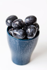 A bunch of big black grapes in a blue cup