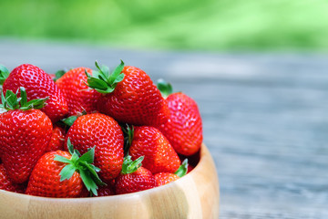 Sweet fresh juicy organic ripe strawberries in wooden bowl on wooden surface outdoors in garden or backyard