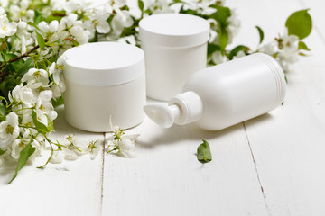 Obraz na płótnie Canvas Skin​care​ packaging​​ set w/ spring flowers on​ white​ background.​ Blank cosmetic bottle/tube of moisturizing cream w/ organic herbal ingredients. Natural beauty​ cosmetology​ concept