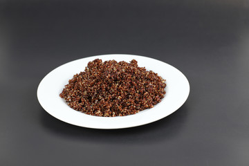 Steamed quinoa on white plate on black background