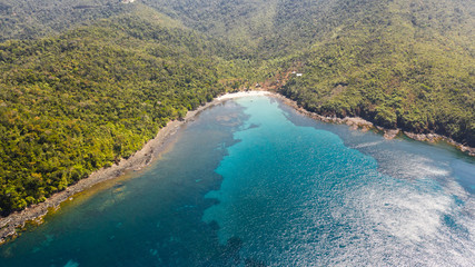 Sea bay with turquoise water and a small white beach.Coast of the island of Camiguin, Philippines.Beautiful lagoon and volcanic island covered with dense forest, view from above.