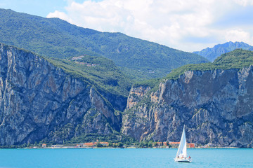 Summer landscape on lake Garda Italy with turquoise water white yacht and green mountains on the banks